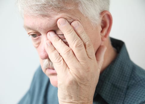 overworked senior rubs an eye in fatigue