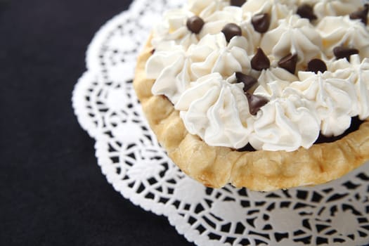 small pie with whipped cream and chocolate chips on a doily