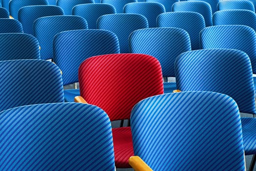 Red seat surrounded by empty blue seats as an eye-catcher