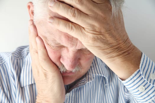older man in pain holds his head with both hands