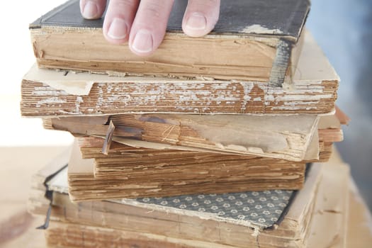 stack of old books with a man's fingers on top