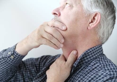 senior man touches area on neck where he feels pain