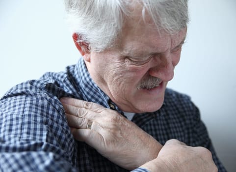 older man grimaces and touches area of pain in his shoulder