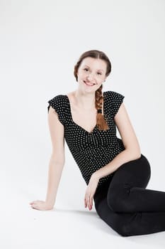 Studio portrait of happy smiling attractive woman with pigtail sitting and supporting herself with arm