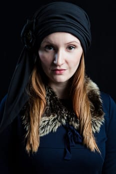 Studio portrait of stylish attractive woman wearing blue outfit and head scarf against dark background