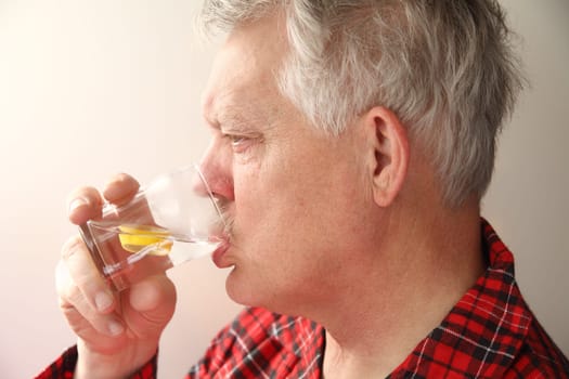 sick senior man in pajamas drinking water with lemon slices