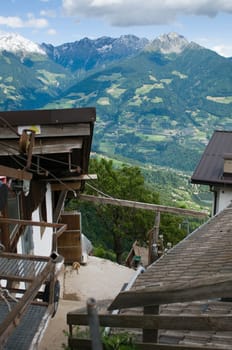 View from above the hochmuth mountain station (village Tyrol / South Tyrol) between the roofs in the direction of the Iffinger mountain range on the other side of the Merano valley in summer