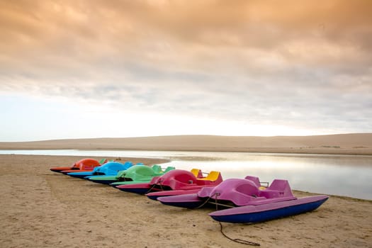 Colorful paddle boats on the sand next to the lagoon water