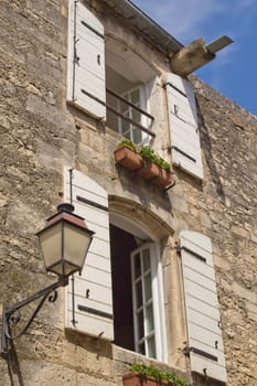 Typical Provencal stone house with white  wooden shutters and flowers in the flower box and also with household lamp. (Provence, France)