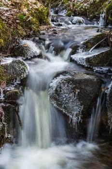 Small waterfall with icicles and ice close up, spring.