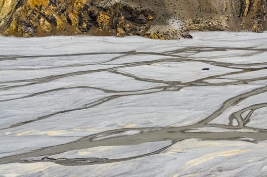 Landscape view of dry eroded river bank with water streams and tractor