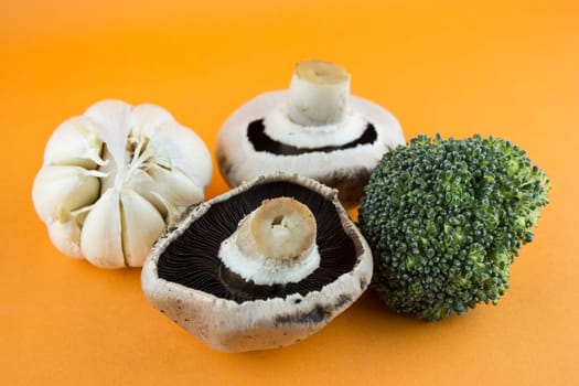 button mushrooms in wooden bowl with garlic, parsley and broccoli on orange background.