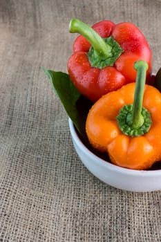 Orange and red sweet pepper with leaves on a Sackcloth background