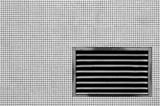 The photograph of a ventilation grille on a wall with mosaic tiles.