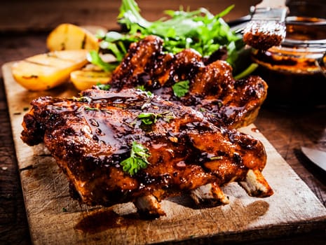 Delicious barbecued ribs seasoned with a spicy basting sauce and served with chopped fresh herbs on an old rustic wooden chopping board in a country kitchen