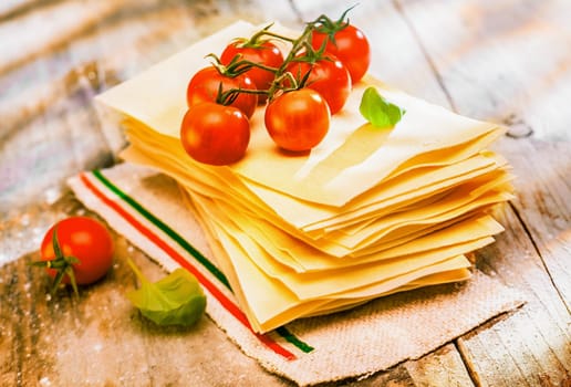 Preparing Italian lasagne with fresh ripe red cherry tomatoes and basil on sheets of dried pasta standing ready on an old rustic wooden kitchen table