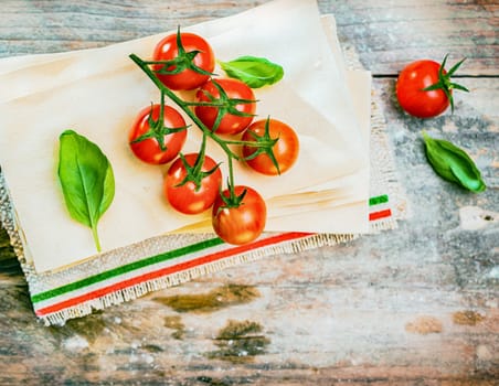 Cherry tomatoes, basil and dried lasagne sheets on an old weathered wooden table in a rustic kitchen ready to be used as ingredients for an Italian pasta dish, view from above