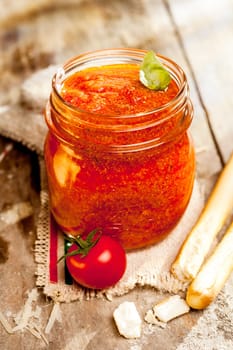 Jar of savory relish or dip with Italian grissini or breadsticks on a cloth with the Italian national colors and fresh tomato