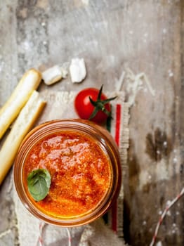 Overhead view of a glass jar of hot spicy tomato relish with grassini or Italian bread sticks on a grungy rustic wooden background with copyspace