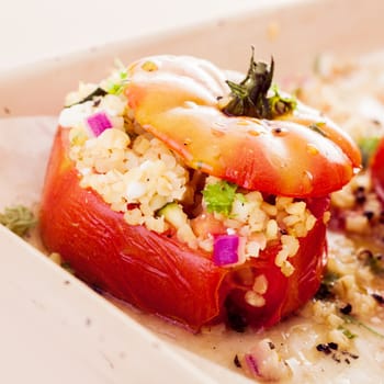 Close up of a tasty ripe red baked tomato stuffed with a savory corn and grain filling with chopped onion and herbs