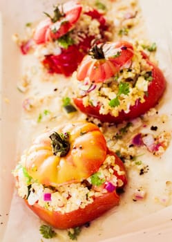 Ripe red baked tomato with savory corn and grain filling with chopped onion and herbs , high angle view of a row of three vegetables