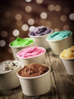 Delicious assortment of party ice cream in individual plastic tubs in multiple colors and flavors with a sparkling bokeh of festive lights