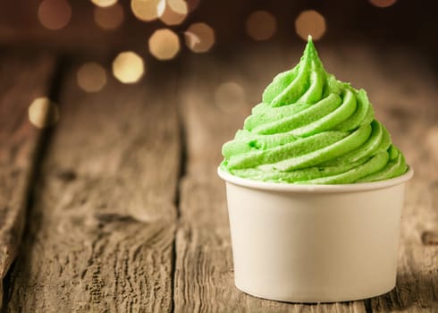 Tub of twirling creamy green Italian ice cream on a rustic wood table with a sparkling bokeh of party lights