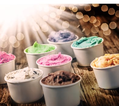 Selection of colorful tubs of frozen multicolored ice cream standing on a rustic wooden table on a hot summer day with a sunbusrt and flare effect