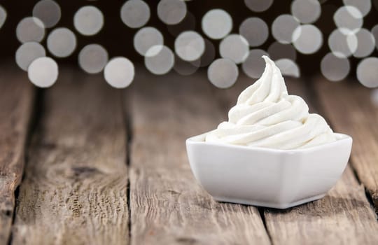 Ceramic dish of twirled delicious tangy lemon sorbet for a refreshing tropical summer dessert on an old rustic restaurant table with a bokeh of twinkling lights