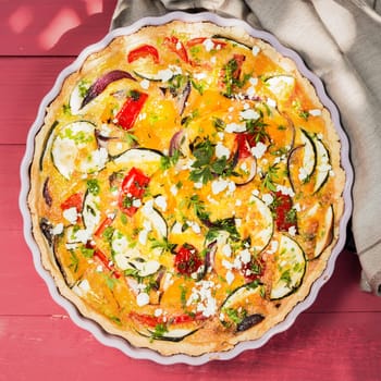 Delicious savory tart or quiche with brinjals or eggplant, pepper, tomato and cheese sprinkled with fresh chopped herbs, overhead view