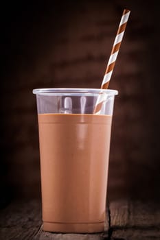 Close up of a glass of chocolate or cacao smoothie with a spiral patterned straw against a dark background