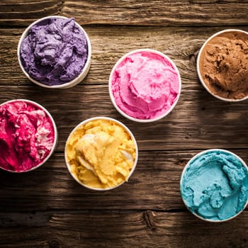 Tasty creamy colorful Italian ice cream in individual tubs for a party or festive occasion served on an old rustic wooden table, overhead view