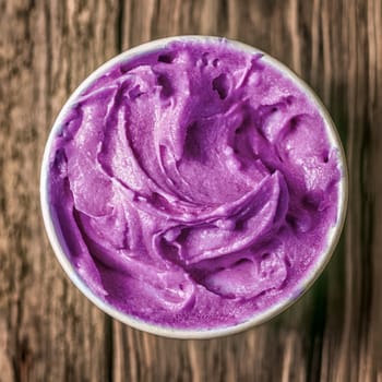Close up overhead view of a takeaway plastic tub of colorful purple berry Italian ice cream on a rustic wood background