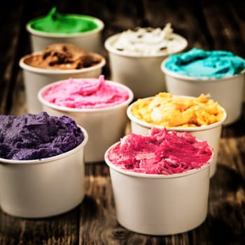 Assorted colorful tubs of fresh dairy ice cream in multiple colors and flavours for a refreshing cold treat on a hot summer day standing on an old wooden table