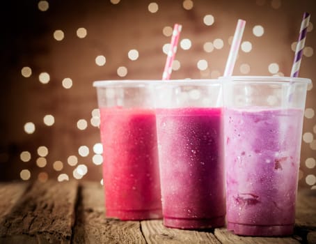 Three different colorful berry smoothies with twinkling party lights standing in a row on a rustic wooden counter top at a restaurant or bar