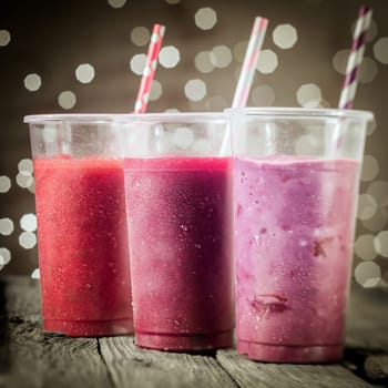Trio of healthy assorted berry smoothies including strawberry and blueberry blended with yogurt or ice cream standing in a row against a bokeh of party lights