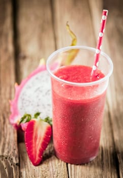 Healthy nutritious tropical smoothie with strawberries and dragon fruit blended with yoghurt or ice cream on a rustic wooden table top
