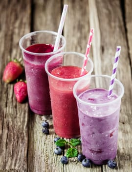 Variety of fresh berry smoothies with a trio of glasses in a row with strawberries and blueberries for a healthy refreshing drink, high angle view on an old wooden surface