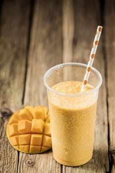 High angle view of a glass of tropical mango smoothie blended with yogurt and ice cream with fresh fruit on an old weathered wooden table with copyspace