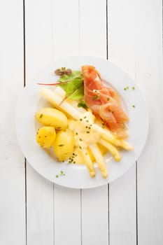 Asparagus and Italian parma or prosciutto ham with mayonnaise served with baby boiled potatoes for a delicious cold summer meal, overhead view on white wooden table with copyspace