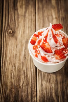 Takeaway strawberries and frozen yohurt topped with sugar pearls in a plastic tub, high angle view on old wooden boards with copyspace