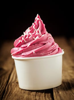 Twirl of delicious berry ice cream or frozen yoghurt in a plastic takeaway tub sprinkled with desiccated coconut against a dark background , close up side view
