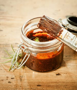 Savoury BBQ basting sauce in a glass jar with a basting brush and sprig of fresh rosemary for seasoning and flavoring the meat