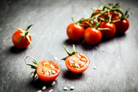 Halved fresh ripe grape tomato showing the pips and juicy pulp in the foreground with a bunch of tomatoes on the vine behind on a dark rustic table, low angle with copyspace