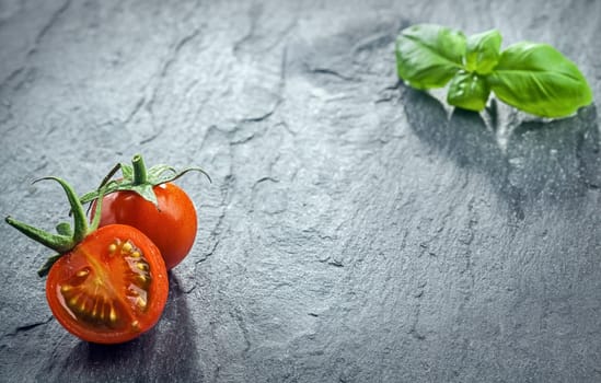 Fresh halved tomato and fresh basil arranged in the the opposite corners of the frame on a dark textured surface at a low angle perspective with copyspace