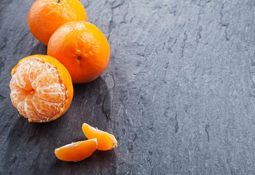 Fresh peeled nectarine for a healthy snack rich in vitamin c with loose segments and two whole fruit arranged as a left-hand border on a slate table with copyspace