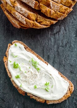 Cream cheese with herbs and seasoning on a slice of fresh rye bread with the sliced loaf alongside, viewed from above with copyspace