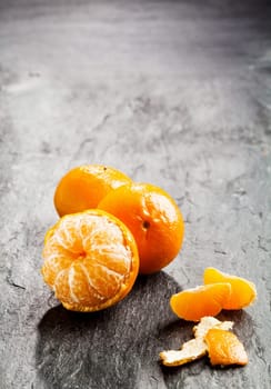 Peeled fresh sweet nectarine, tangerine or clementine with scattered loose peel and segments on a dark background with copyspace