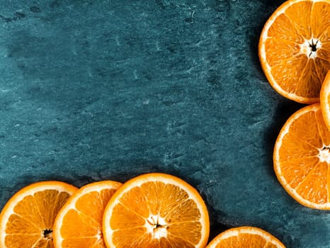 Border of fresh juicy orange slices arranged on two sides on a dark textured slate background with copyspace for your text