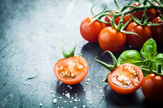 Fresh grape tomatoes with basil and coarse salt for use as cooking ingredients with a halved tomato in the foreground with copyspace